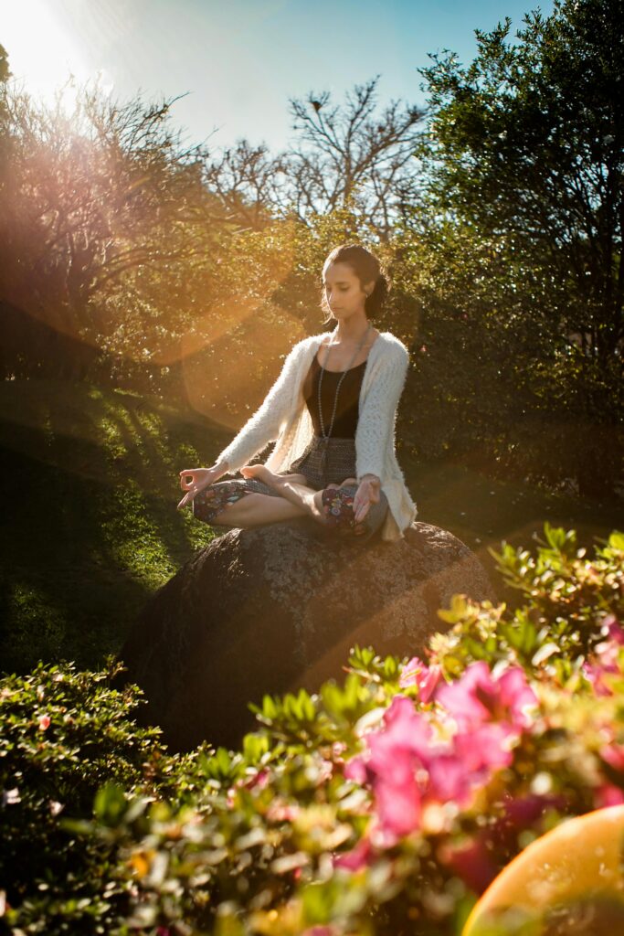 pexels-photo-2597205-2597205 Woman in tranquil meditation pose outdoors, bathed in sunlight, surrounded by lush greenery.